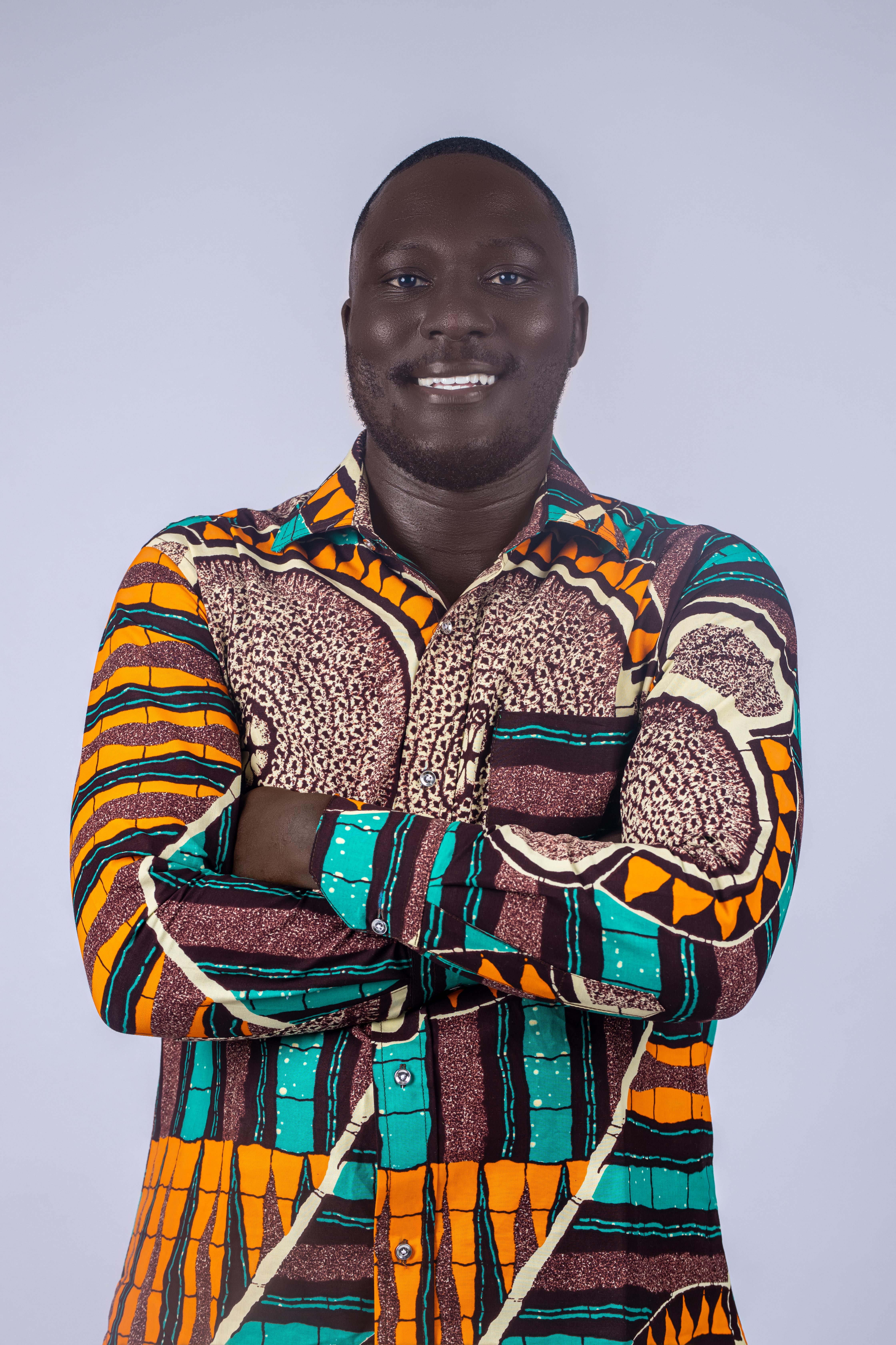 Smiling man in vibrant traditional shirt with arms crossed against a gray studio background.