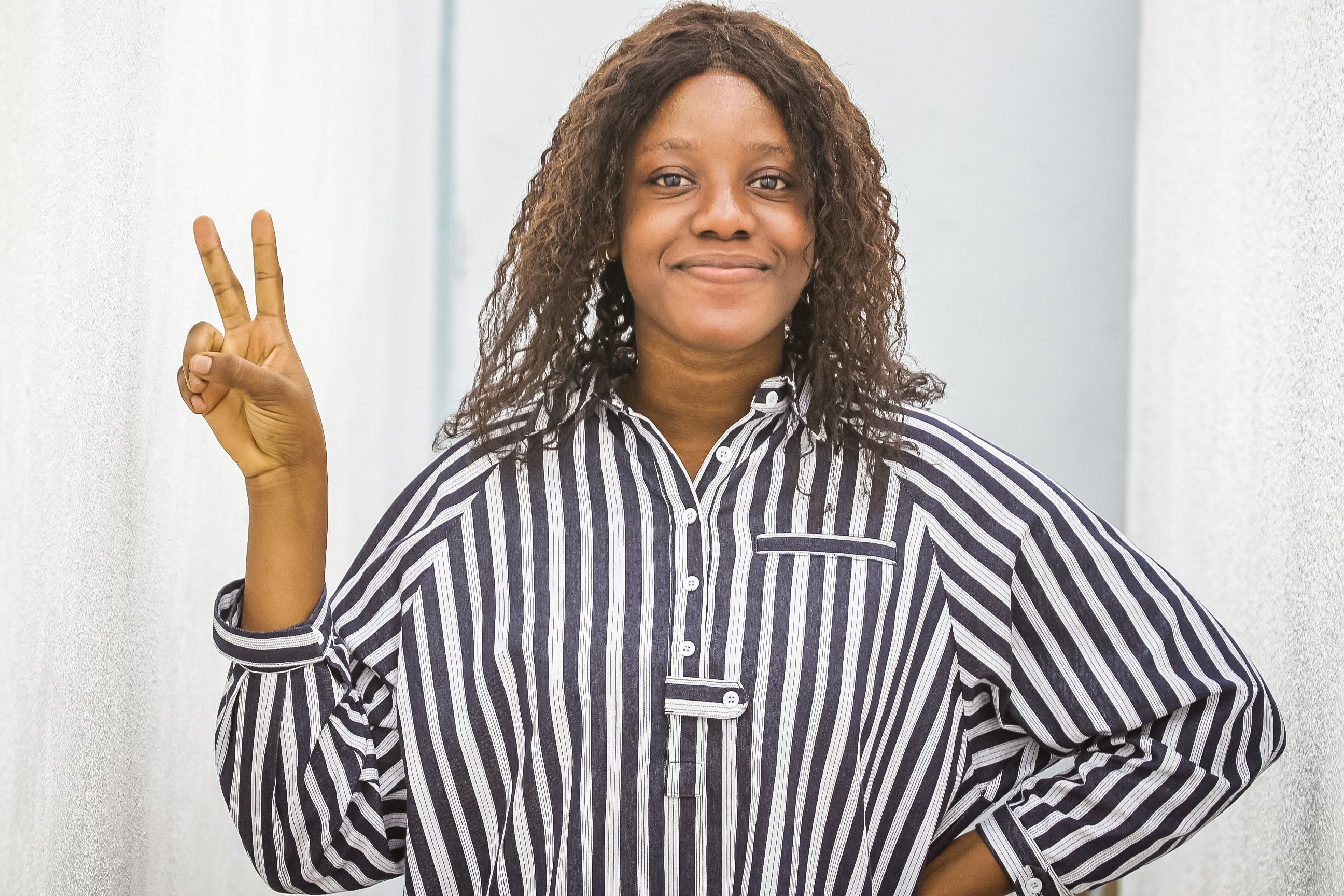 Portrait of a smiling woman making a peace sign indoors wearing a striped shirt.